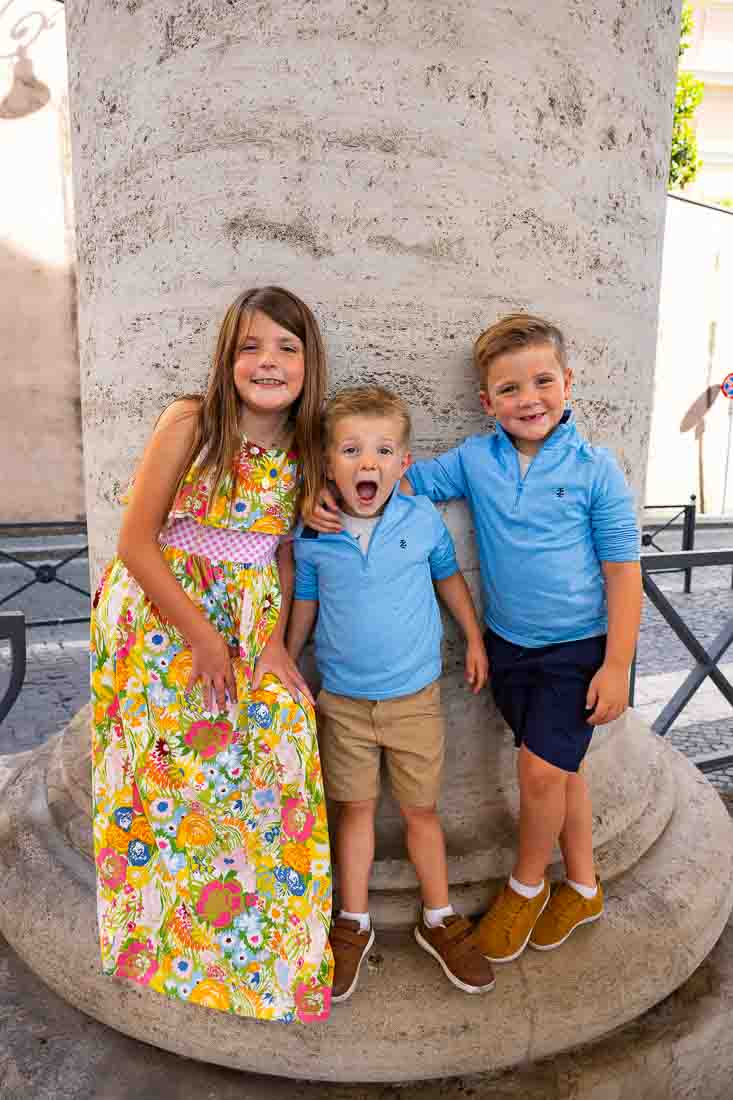 Children playing between the colonnade columns in the area surrounding Saint Peter’s Basilica during a candid outdoor photo shoot in soft natural light with architectural elements in the background