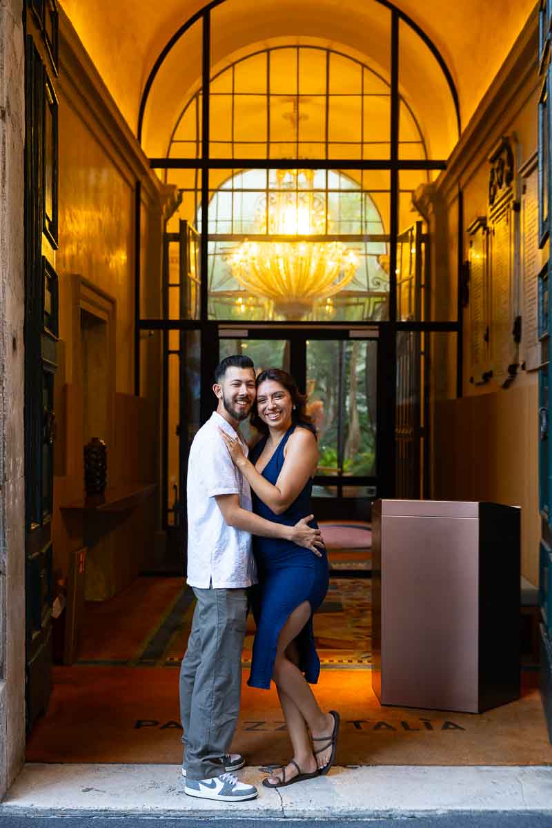 Romantic portrait of the newly engaged couple standing by a grand hotel entrance, featuring elegant architectural details and a natural photography style capturing the atmosphere of their morning walk.