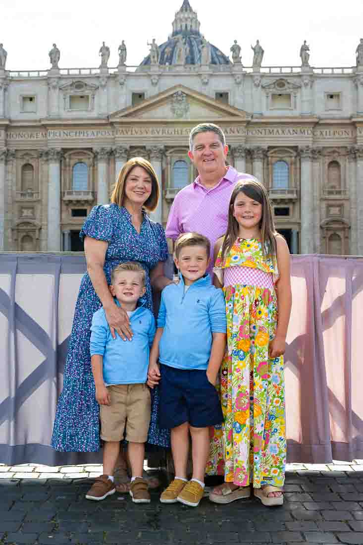 Grandparents standing together with their grandchildren beneath the colonnade near the basilica during a portrait photo shoot under soft natural light with architectural surroundings and background view