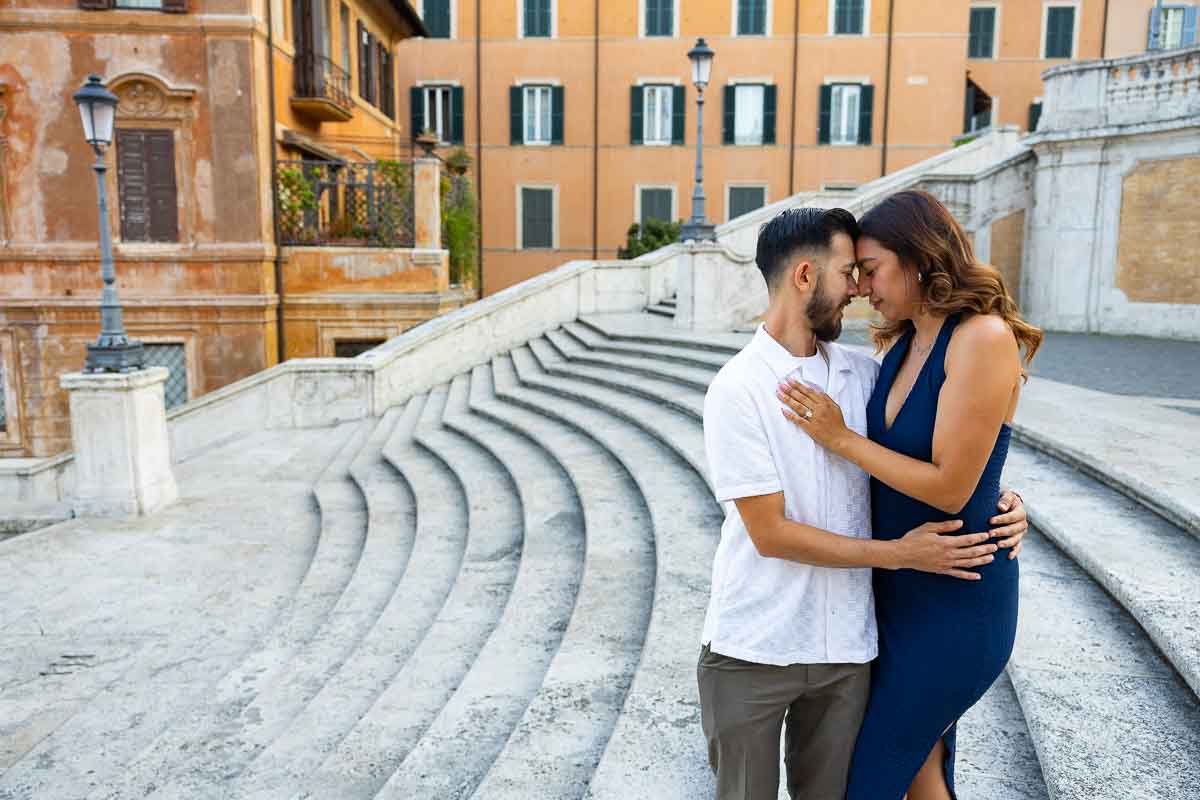 Romantic portrait of the engaged couple standing face to face above Piazza di Spagna, framed by the sweeping curved staircase to create a striking geometric composition with layered architectural lines.