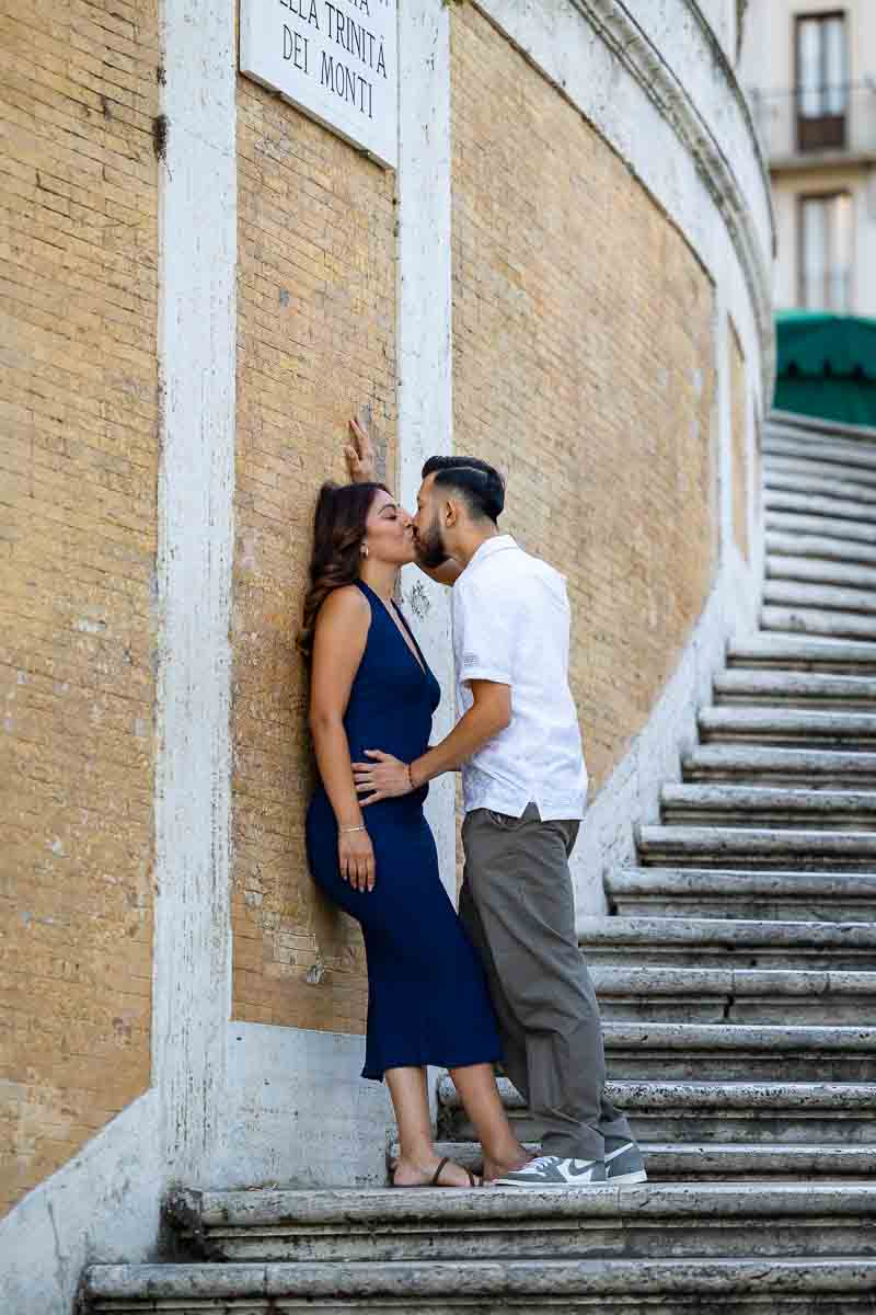 Romantic snapshot of the couple kissing at the base of the staircase, using the repeating curves and symmetrical lines to create a dynamic visual composition with a creative portrait style.