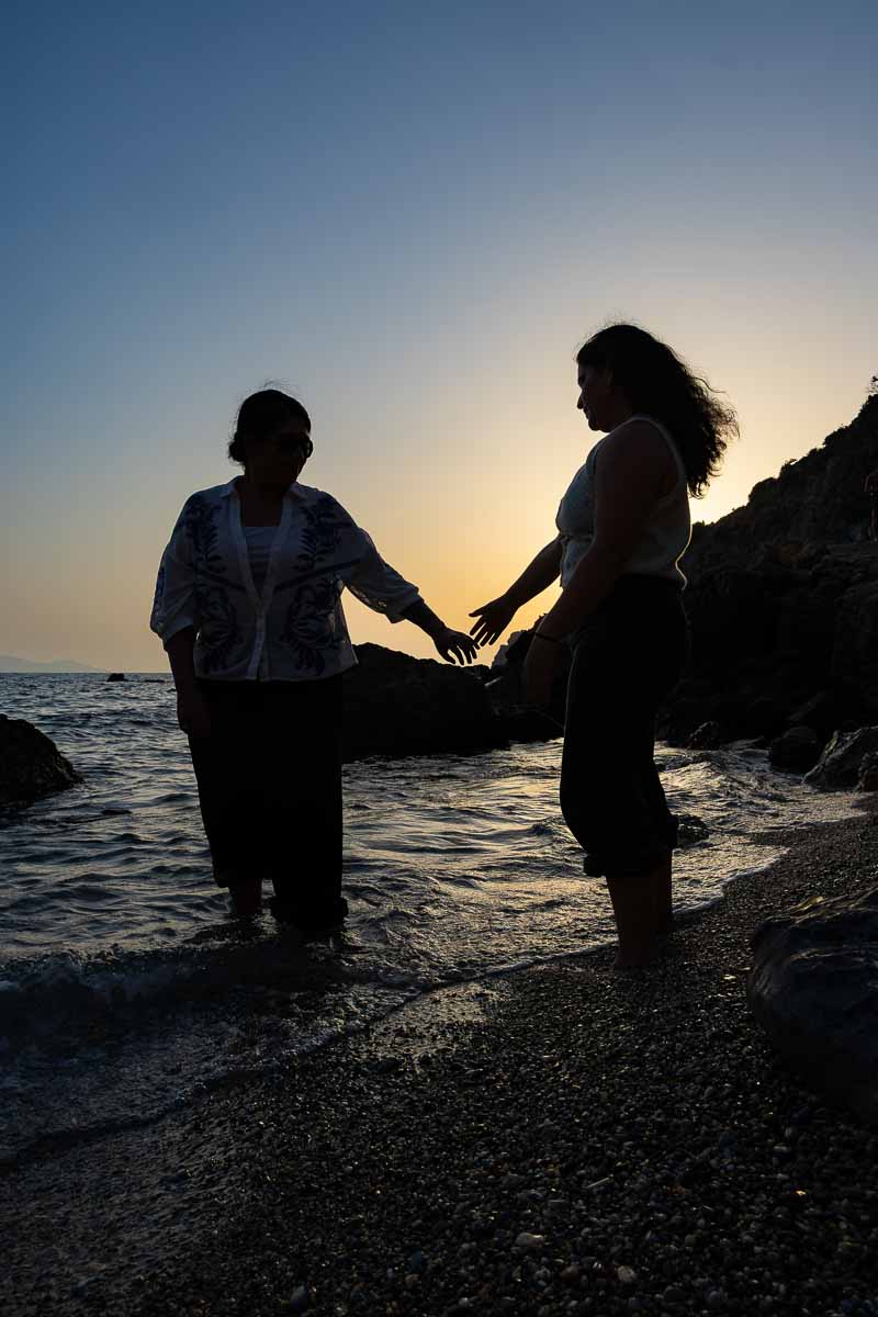 Artistic silhouette photograph of an engaged couple holding hands along the shoreline as the evening sun sets over the Tuscan coastline.
