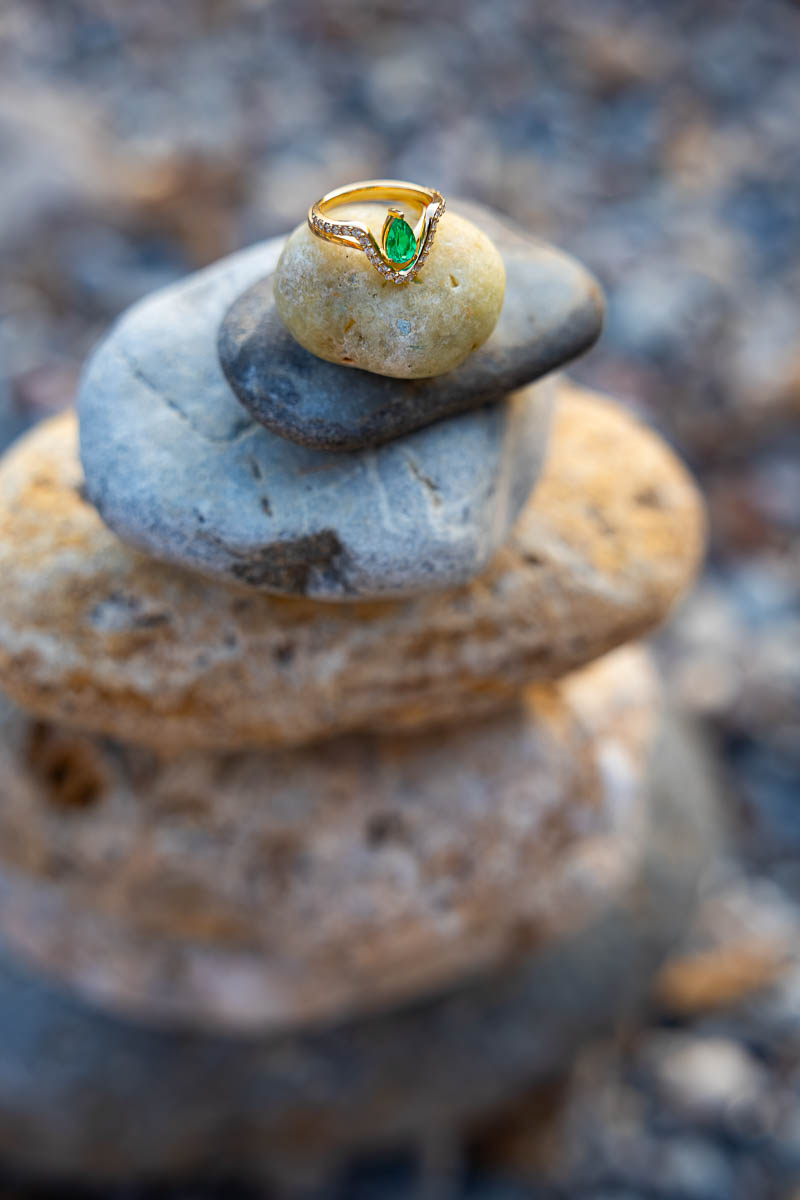 Creative still-life photography of a diamond engagement ring displayed on balanced coastal stones, highlighting fine detail against the natural textures of the beach.