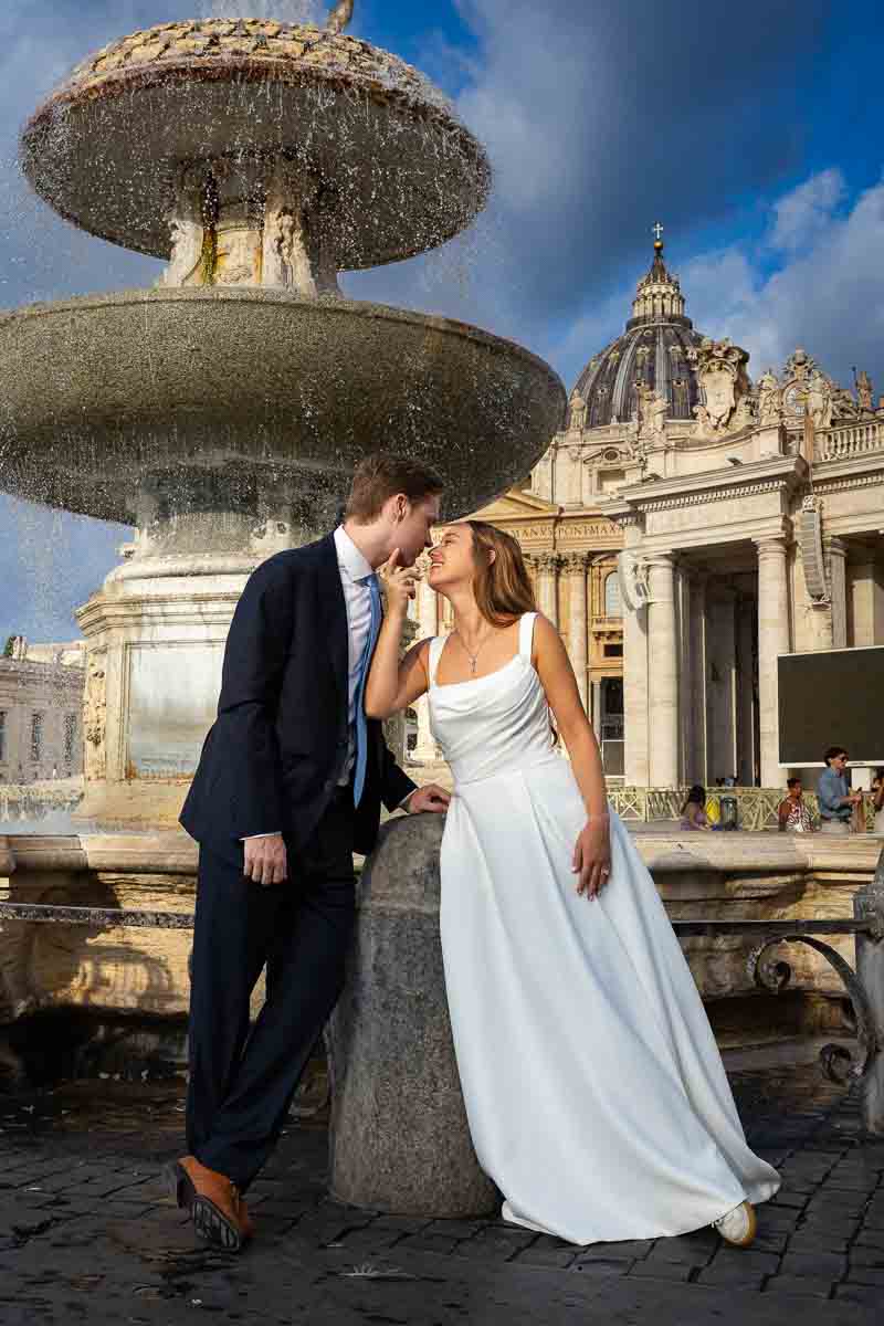 Romantic scene beside an ornate stone fountain, composed as a candid-style portrait with the curved arcades extending into the background