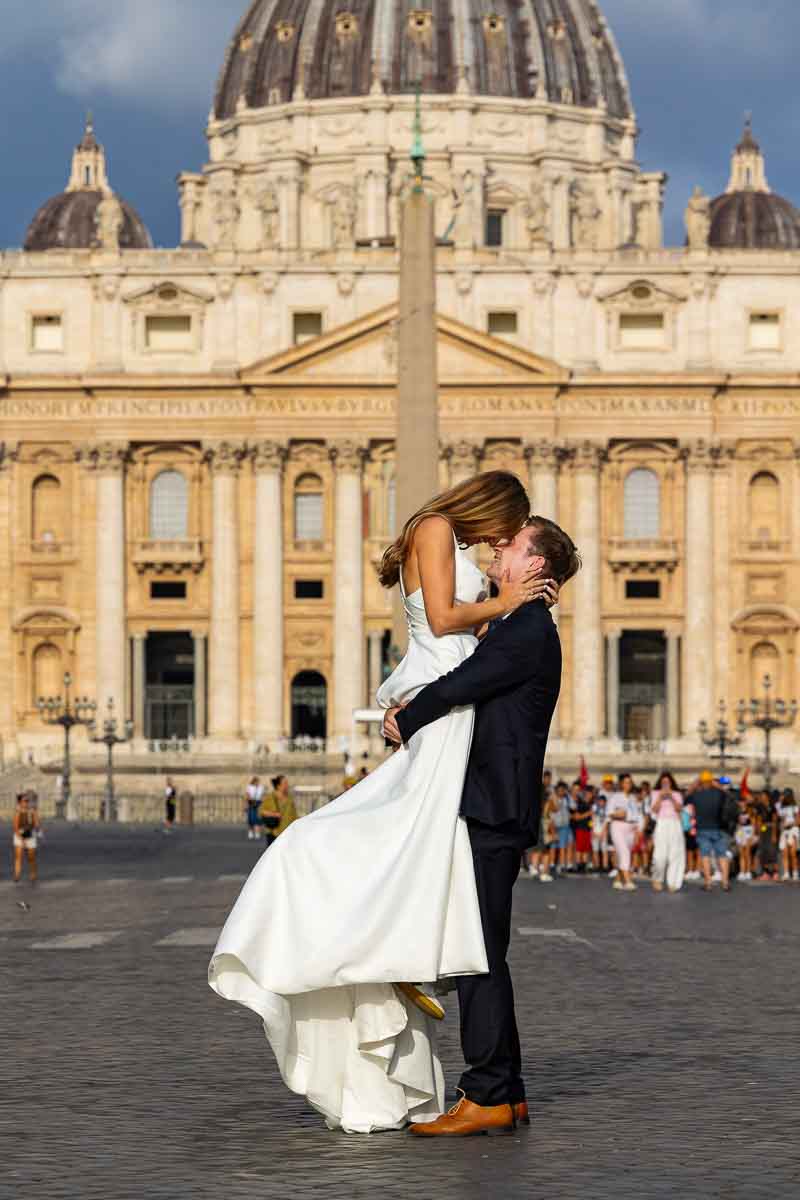 Newly married pair standing in the vast piazza beneath the cathedral, framed in a wide photograph that includes the surrounding square and historic buildings