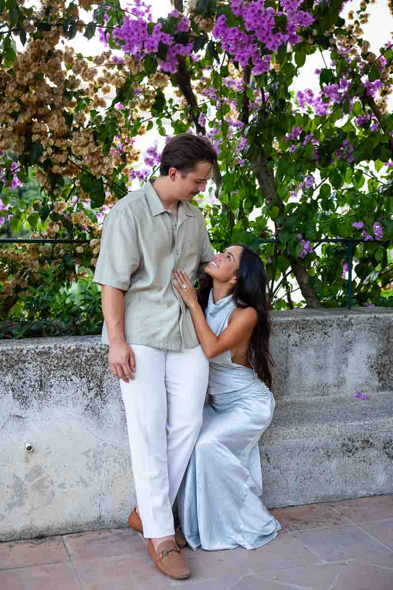 A relaxed lifestyle portrait of a couple sitting together by a blooming bougainvillea plant within the scenic historical grounds.