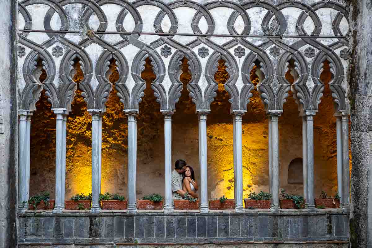 A perfectly executed editorial portrait of a couple within the illuminated architectural ruins of Villa Rufolo at dusk.